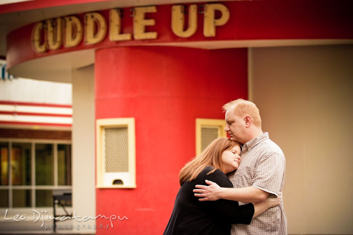 Engaged guy hugging his fiancée by the cuddle up sign. Pre wedding engagement photo session at Glen Echo Park Maryland by wedding photographer Leo Dj Photography