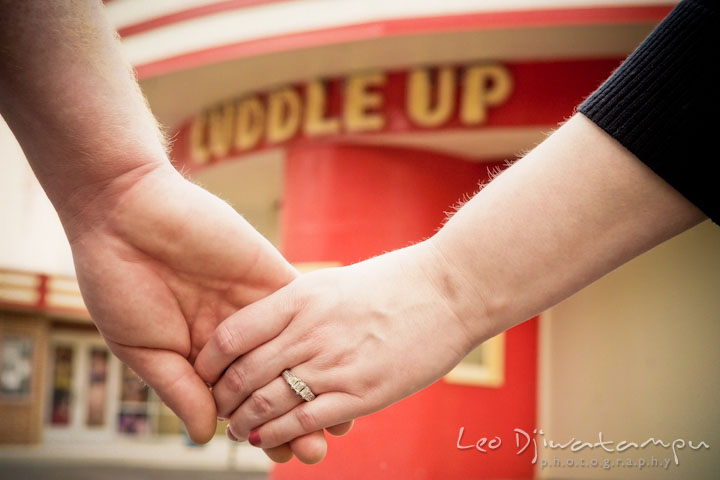 Engaged girl holding her fiancé and showing the engagement ring by the cuddle up sign. Pre wedding engagement photo session at Glen Echo Park Maryland by wedding photographer Leo Dj Photography