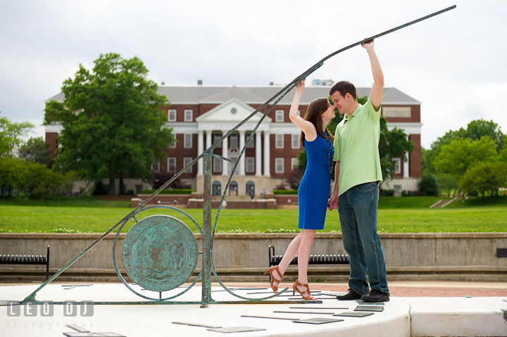 Engaged girl and her fiancé holding sun dial at the McKeldin Library Mall. Pre-wedding or engagement photo session at University of Maryland at College Park campus by wedding photographers of Leo Dj Photography.