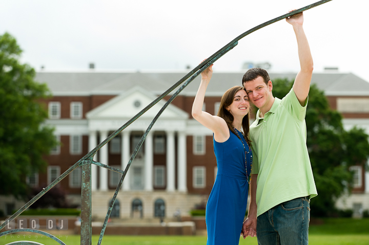Engaged guy and his fiancée holding sun dial at the McKeldin Library Mall. Pre-wedding or engagement photo session at University of Maryland at College Park campus by wedding photographers of Leo Dj Photography.