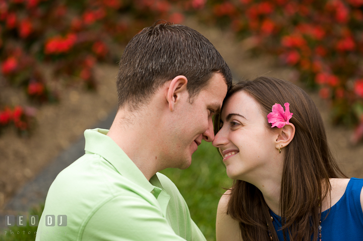 Engaged girl with pink azalea on her ear touching noses with her fiancé. Pre-wedding or engagement photo session at University of Maryland at College Park campus by wedding photographers of Leo Dj Photography.
