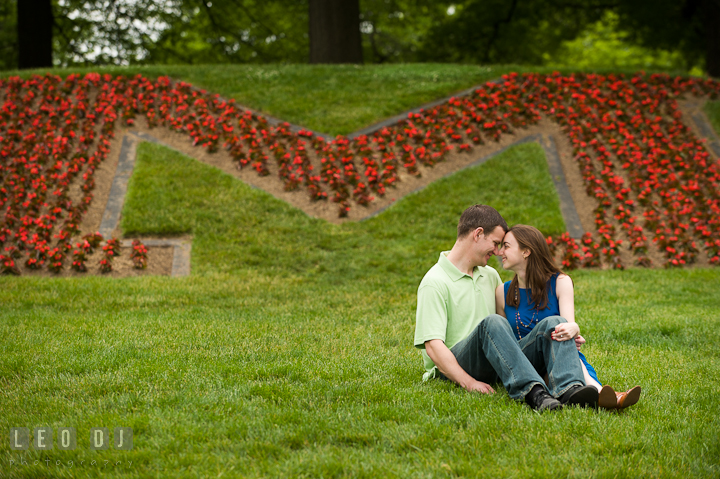 Engaged couple sitting by a big M flower bed. Pre-wedding or engagement photo session at University of Maryland at College Park campus by wedding photographers of Leo Dj Photography.