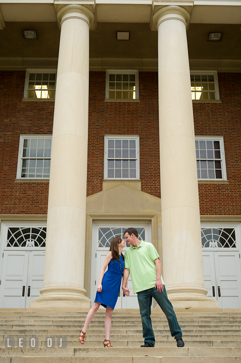 Engaged guy holding hands with his fiancée by a campus building. Pre-wedding or engagement photo session at University of Maryland at College Park campus by wedding photographers of Leo Dj Photography.