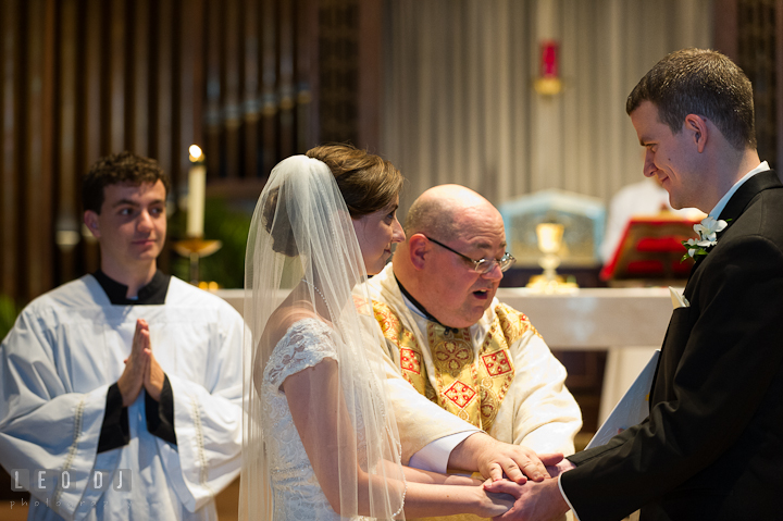 Bride and Groom smiling while blessed by the Priest. Saint John the Evangelist church wedding ceremony photos at Severna Park, Maryland by photographers of Leo Dj Photography. http://leodjphoto.com