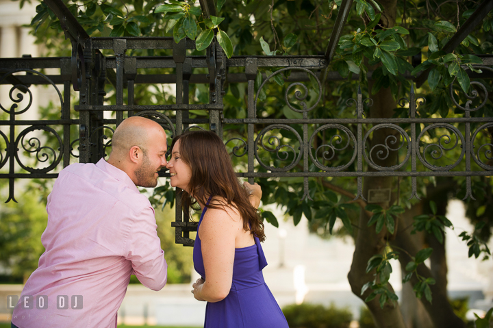 Engaged guy hanging on bench poles and almost kiss his fiancée by the Capitol Hill. Washington DC pre-wedding engagement photo session, by wedding photographers of Leo Dj Photography. http://leodjphoto.com