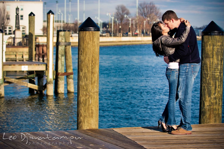 Engaged couple kissing by a downtown marina pier pole. City or urban setting pre-wedding or engagement photo session at Annapolis, by Annapolis wedding photographer, Leo Dj Photography.