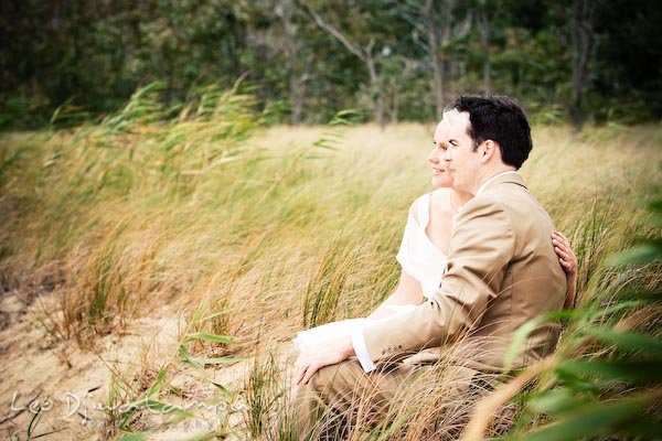 bride groom sitting together on sand by tall grasses enjoying the view. Annapolis Kent Island MD Modern Intimate Candid Posed Photojournalistic Style Wedding Photographer