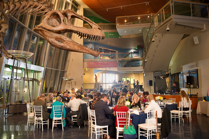 View of guests eating at their tables in the main hall with a T-Rex bones and skull in the foreground. Baltimore Maryland Science Center wedding reception and ceremony photo, by wedding photographers of Leo Dj Photography. http://leodjphoto.com