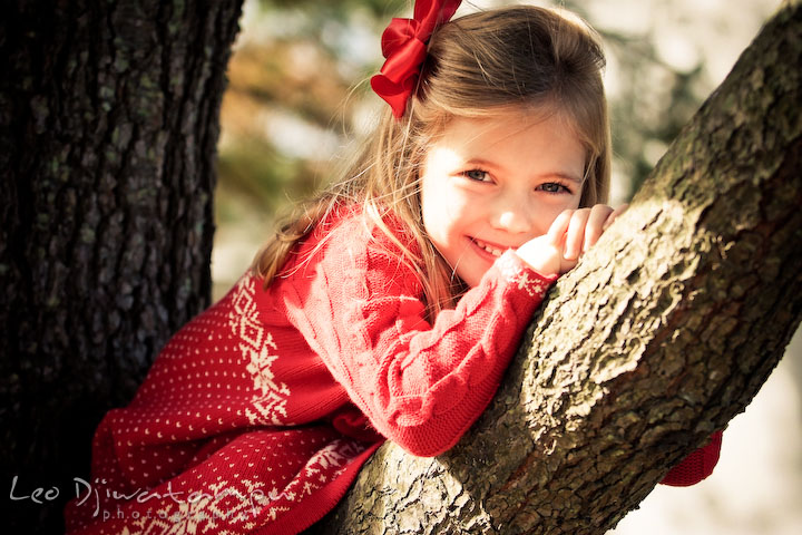 girl with red ribbon and dress, posing on a tree branch. Candid children photographer St Michael Tilghman Island MD