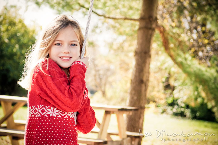 blond girl in red dress playing swing, smiling. Candid children photographer St Michael Tilghman Island MD