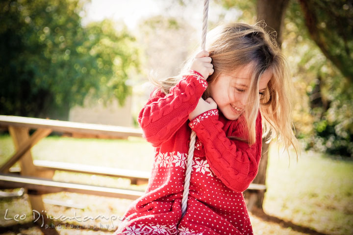 girl in red dress playing swing and laughing. Candid children photographer St Michael Tilghman Island MD