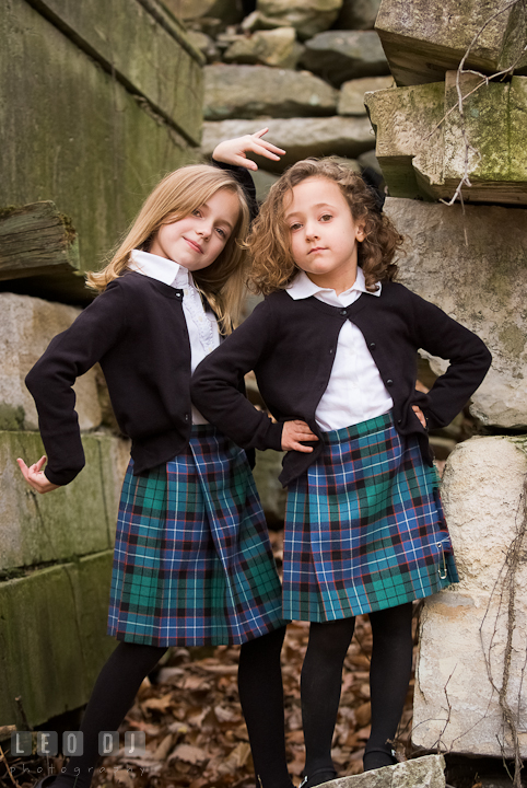 Two sisters, one blonde, one curly brunette, posing by stone ruins. Washington DC fun and candid children lifestyle photo session of Helena and Vivian by photographers of Leo Dj Photography.