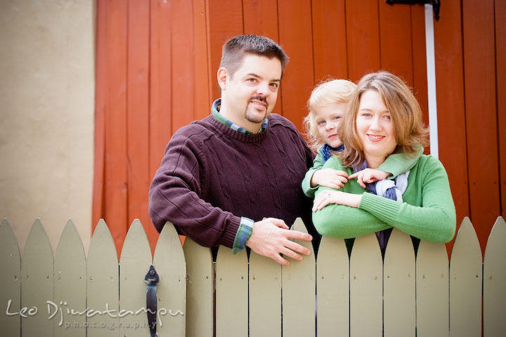 Mom, dad, and daughter posing by a green picket fence. Annapolis Maryland candid lifestyle family portrait photography