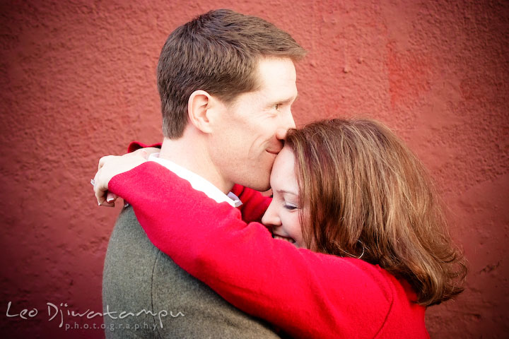 Guy kissed girls forehead, red brown wall background. Urban city theme engagement session photographer Annapolis MD