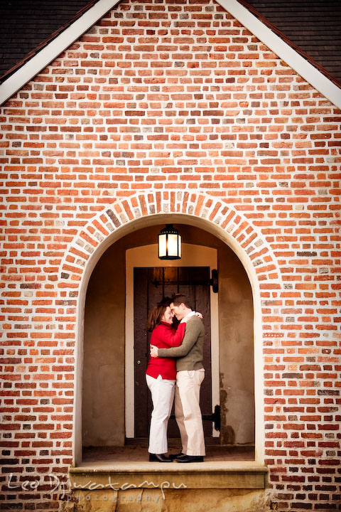 Engaged couple hugging under archway of old brick building. Urban city theme engagement session photographer Annapolis MD