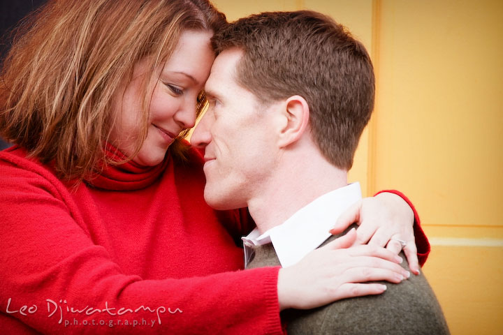 Engaged couple romantically cuddling by a yellow door. Urban city theme engagement session photographer Annapolis MD