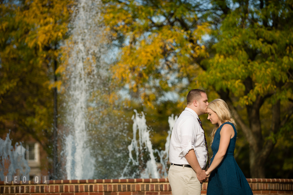 Engaged girl by the water fountain kissed on the forehead by her fiancé. Gettysburg PA pre-wedding engagement photo session, by wedding photographers of Leo Dj Photography. http://leodjphoto.com