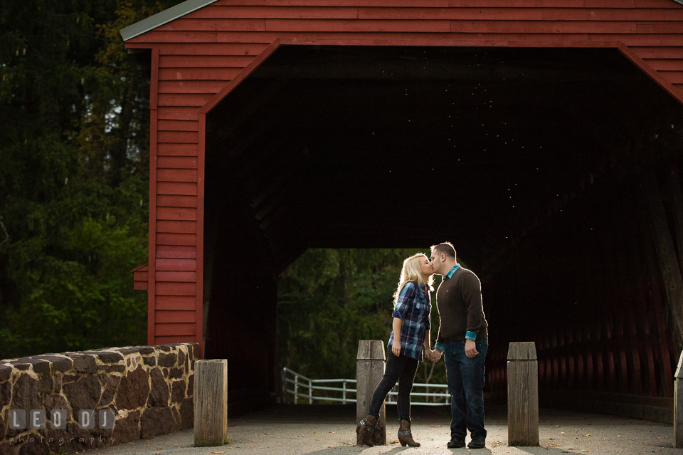 Engaged couple by the Sachs Covered Bridge holding hands and kissing. Gettysburg PA pre-wedding engagement photo session, by wedding photographers of Leo Dj Photography. http://leodjphoto.com