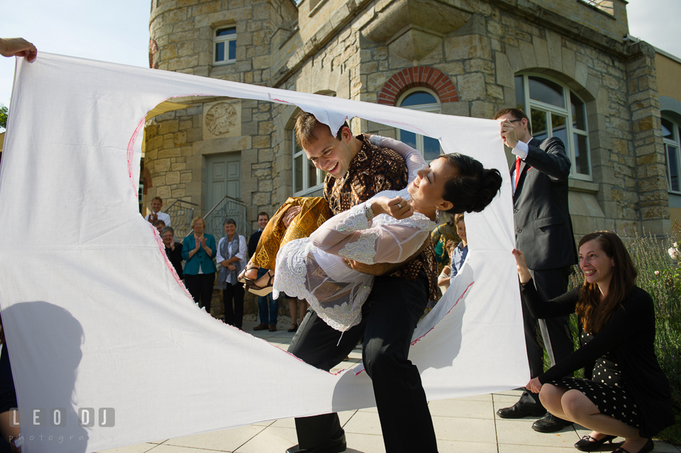 Groom carrying the Bride over the hearty hole in a sheet of fabric. Landgrafen Restaurant, Jena, Germany, wedding reception and ceremony photo, by wedding photographers of Leo Dj Photography. http://leodjphoto.com