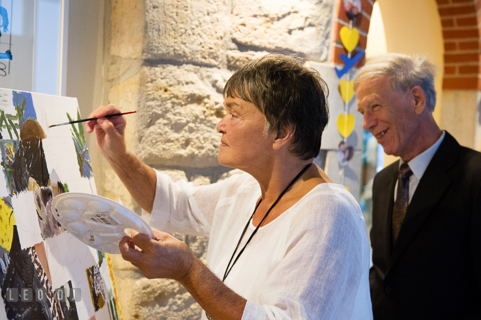 Mother of the Groom having fun painting on the canvas watched by Father of Groom. Landgrafen Restaurant, Jena, Germany, wedding reception and ceremony photo, by wedding photographers of Leo Dj Photography. http://leodjphoto.com