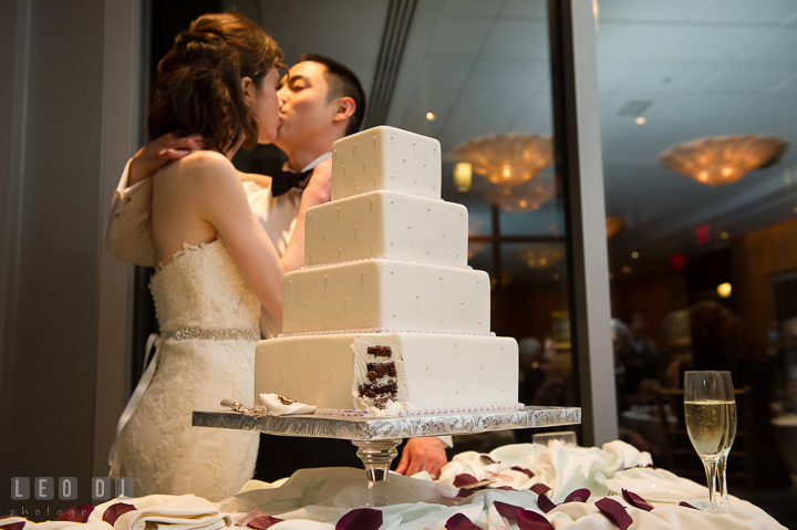 Cut wedding cake with Bride and Groom kissing in the background. Falls Church Virginia 2941 Restaurant wedding reception photo, by wedding photographers of Leo Dj Photography. http://leodjphoto.com