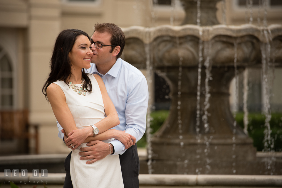 Engaged man hugging and kissing his fiancée by a fountain. Annapolis Eastern Shore Maryland pre-wedding engagement photo session at downtown, by wedding photographers of Leo Dj Photography. http://leodjphoto.com