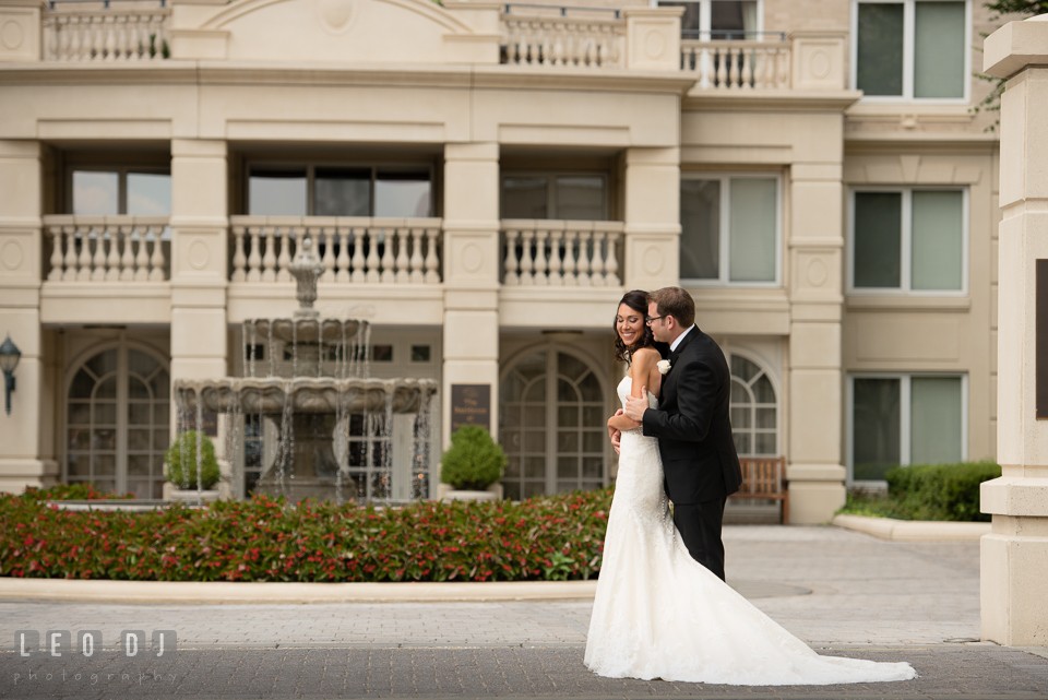 Groom hugging Bride in front of a water fountain. Loews Annapolis Hotel Maryland wedding, by wedding photographers of Leo Dj Photography. http://leodjphoto.com