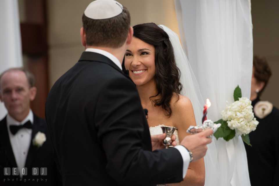 Bride smiling as Groom lift up candle and wine cup, traditional Jewish wedding ceremony. Loews Annapolis Hotel Maryland wedding, by wedding photographers of Leo Dj Photography. http://leodjphoto.com