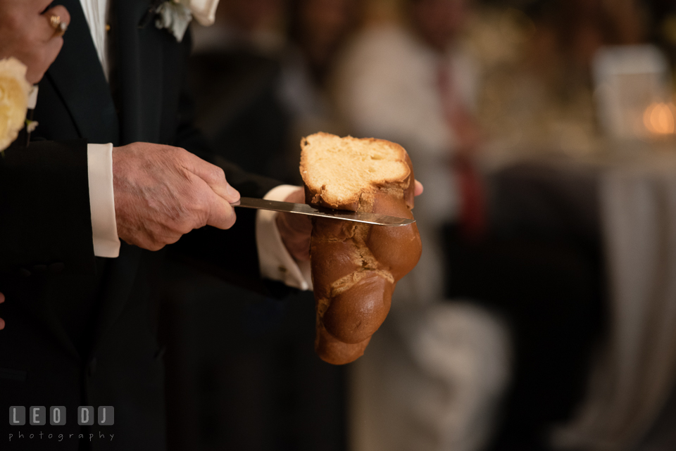 Grandfather cutting bread during blessing over challah. Loews Annapolis Hotel Maryland wedding, by wedding photographers of Leo Dj Photography. http://leodjphoto.com