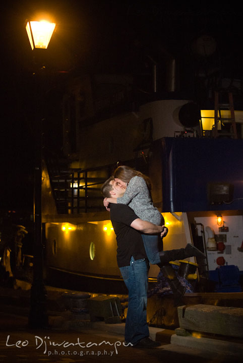 Engaged guy lifted up his fiancée and kissed by the boat. Fells Point Baltimore Maryland pre-wedding engagement photo session with their dog pet by wedding photographers of Leo Dj Photography