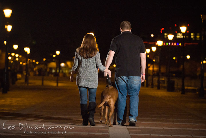 Engaged girl and her fiancé walking their dog in the evening. Fells Point Baltimore Maryland pre-wedding engagement photo session with their dog pet by wedding photographers of Leo Dj Photography