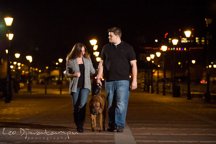 Engaged guy and girl walking with their dog in the evening. Fells Point Baltimore Maryland pre-wedding engagement photo session with their dog pet by wedding photographers of Leo Dj Photography