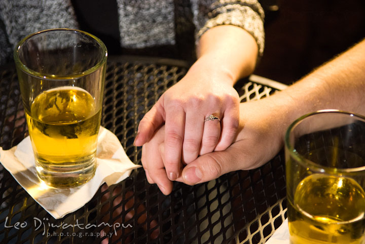 Engaged couple holding hands, showing the wedding ring with glasses of beers. Fells Point Baltimore Maryland pre-wedding engagement photo session with their dog pet by wedding photographers of Leo Dj Photography