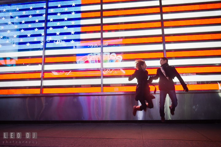 Engaged guy and girl jumping in front of an American flag light display. Pre-wedding engagement photo session at New York City, NY, by wedding photographers of Leo Dj Photography. http://leodjphoto.com