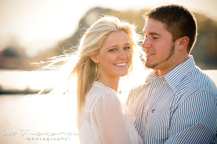 Engaged girl smiling while her hair is blown by the wind. Her fiancé looked at her. Stevensville, Kent Island, Maryland, Pre-Wedding Engagement Photographer, Leo Dj Photography