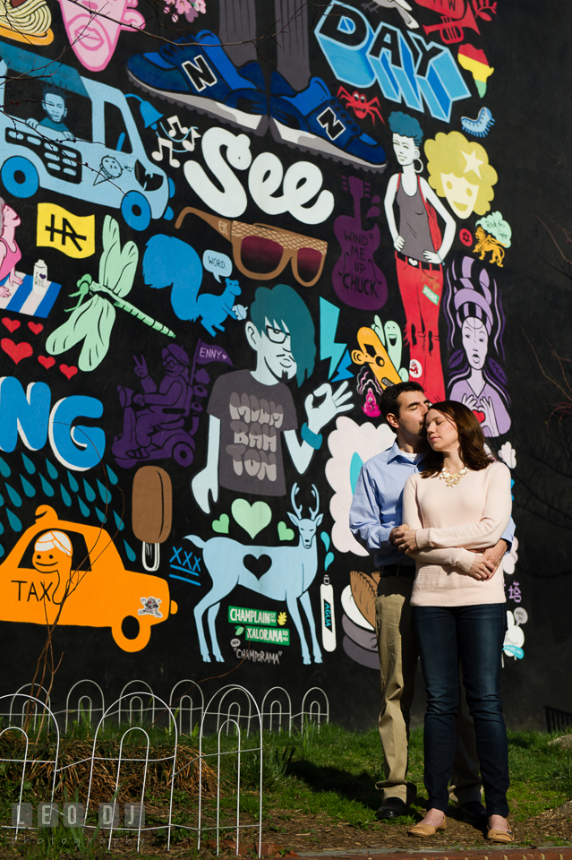 Engaged couple hugged and kissed in front of a wall mural. Washington DC pre-wedding engagement photo session at Adams Morgan and the Smithsonians, by wedding photographers of Leo Dj Photography. http://leodjphoto.com