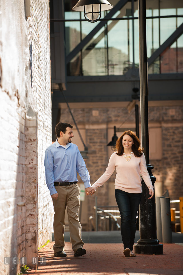 Engaged couple holding hands, walking together on a sidewalk, and smiling. Washington DC pre-wedding engagement photo session at Adams Morgan and the Smithsonians, by wedding photographers of Leo Dj Photography. http://leodjphoto.com