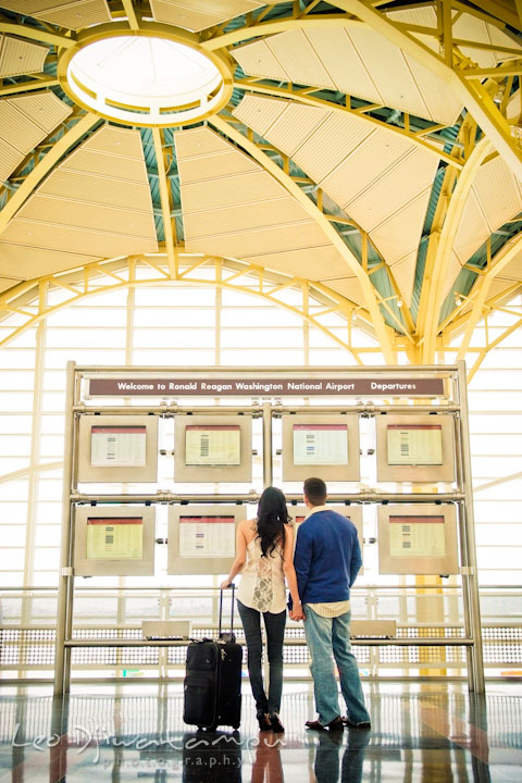 Engaged fiancé and fiancée looking at departure schedule screens. Pre wedding engagement photo Washington DC Smithsonians museum and Ronald Reagan Washington National Airport DCA, by wedding photographer Leo Dj Photography