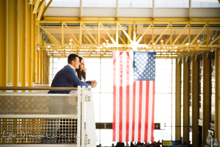 Engaged guy holding fiancée's hand on balcony. American flag in the background. Pre wedding engagement photo Washington DC Smithsonians museum and Ronald Reagan Washington National Airport DCA, by wedding photographer Leo Dj Photography