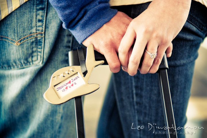 Engaged couple holding hands showing diamond engagement ring and suitcase