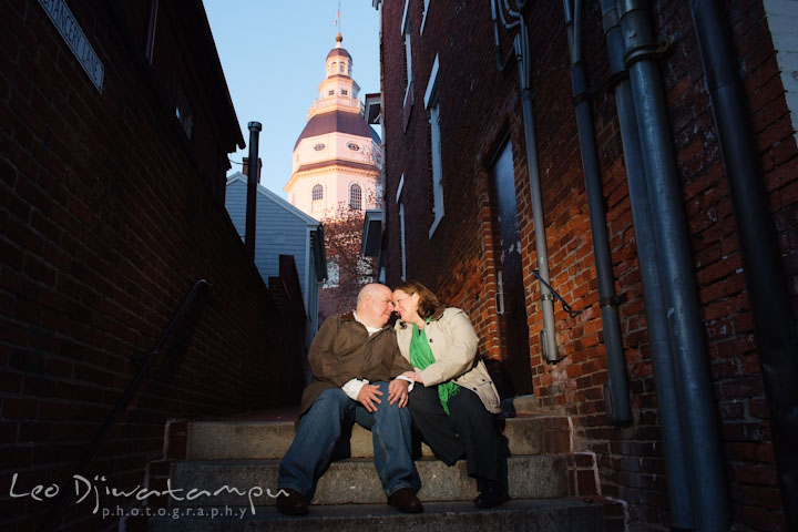 Engaged couple sitting on stairs, with the Annapolis State House in the background. Annapolis Downtown USNA Pre-wedding Engagement Photographer, Leo Dj Photography