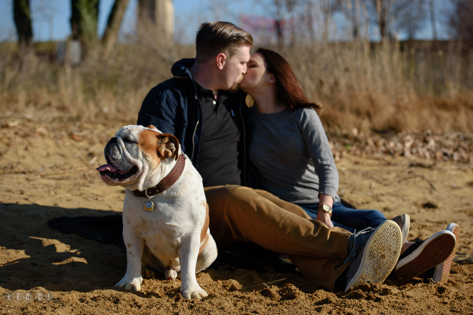 Jonas Green Park Annapolis Maryland engaged couple kissing on beach while dog looking away photo by Leo Dj Photography.