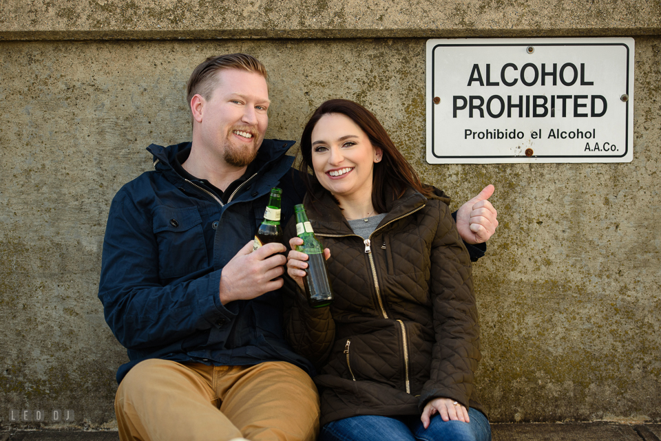 Jonas Green Park Annapolis Maryland engaged man and fiancee holding beer bottles by an alcohol prohibited sign photo by Leo Dj Photography.