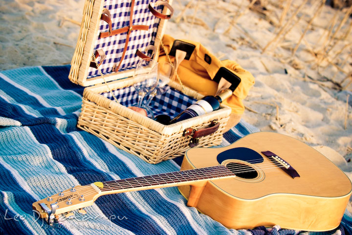 wine bottle, glasses, apple inside a picnic box and guitar on a blanket. Romantic engagement session on beach Kent Island Maryland