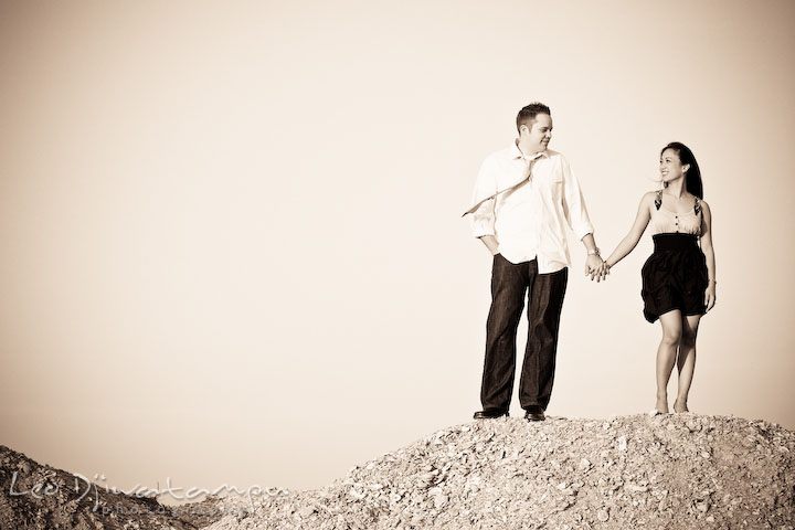 guy and girl holding hands, looking at each other, sepia color. Romantic engagement session on beach Kent Island Maryland