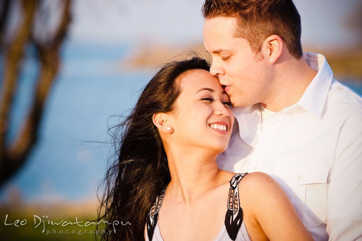 guy kissed girl on her forehead. girl smiling. Romantic engagement session on beach Kent Island Maryland