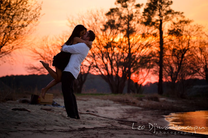 engaged couple hugging, kissing on the beach with warm amber sunset. Romantic engagement session on beach Kent Island Maryland