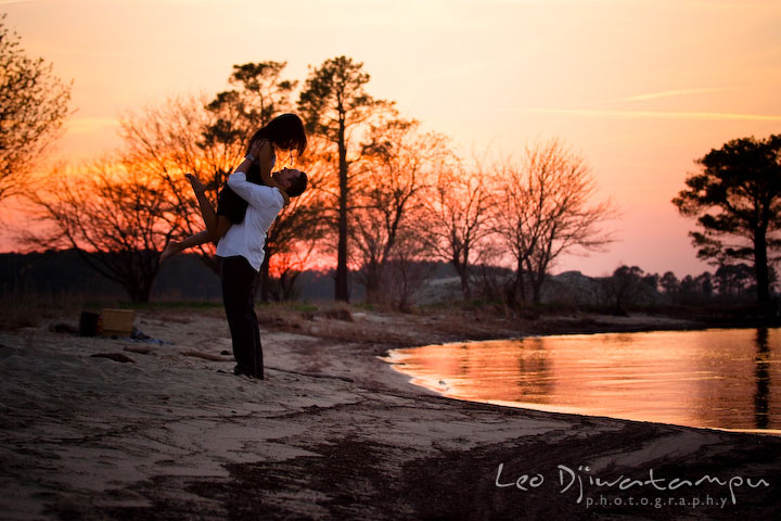 engaged couple, guy lift up girl on the air, warm amber color sunset. Romantic engagement session on beach Kent Island Maryland