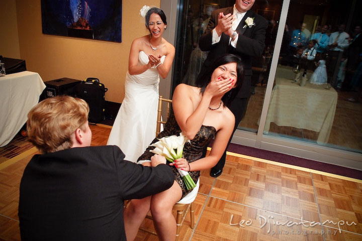 Girl covers her mouth laughing when guy put garter on her leg. Bride and groom laughing and clapping hands. Falls Church Virginia 2941 Restaurant Wedding Photographer