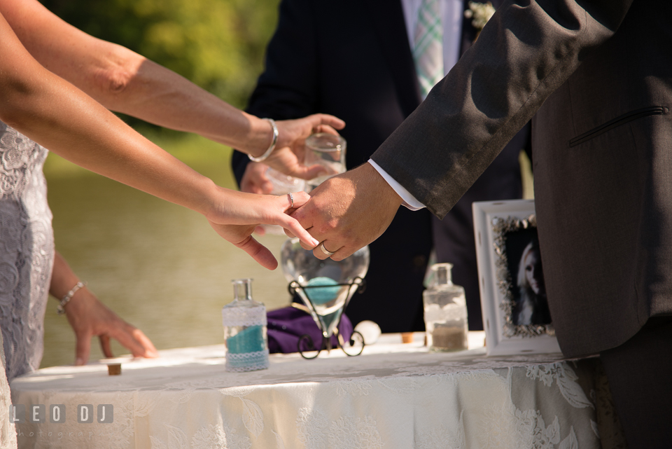 The Oaks Waterfront Inn Bride and Groom holding hands while parents pouring unity sand photo by Leo Dj Photography